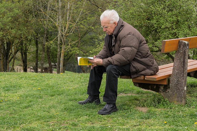 Elderly person sitting on bench and reading